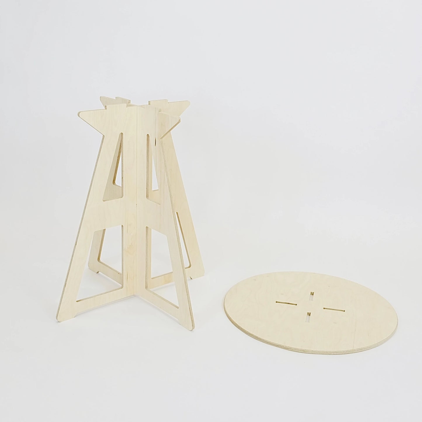 A simple modern pale wooden small table top and legs. It has a round top which lays on the floor, and triangle legs which have slotted together in a cross shape, the base is wider than the top. The top also features four grooves where the legs would slot into the top.