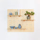 A medium pale wooden pegboard with many drilled holes, three shelves & pegs faces front on. Various blue accessories are displayed on the board.