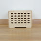 Birch plywood wooden crate with 5 rows of lozenge shape cutouts running vertically & wooden lid against a white wall