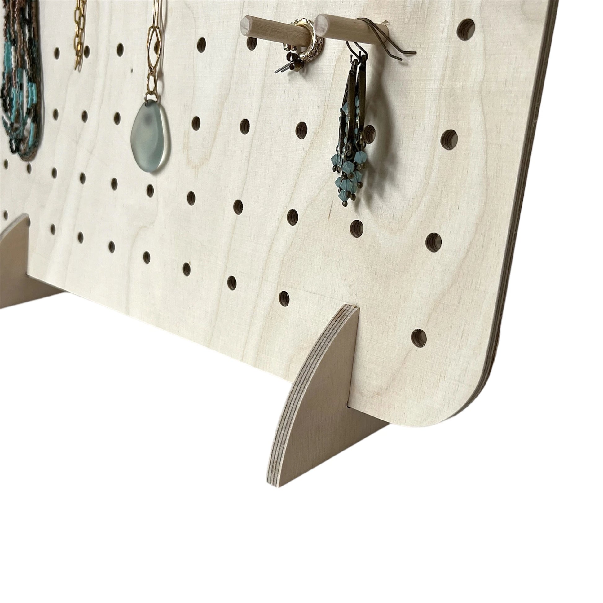 Close up of pale wooden pegboard facing to left.  Pegboard has jewellery hanging from the pegs.
