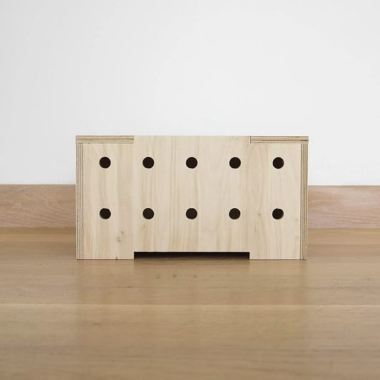 A simple pale wooden crate with two rows of holes in front and lid. It faces front on and sits on wooden floor.