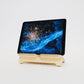 Pale wooden tablet stand with tablet displaying the cosmos, angled to the left on a white background.