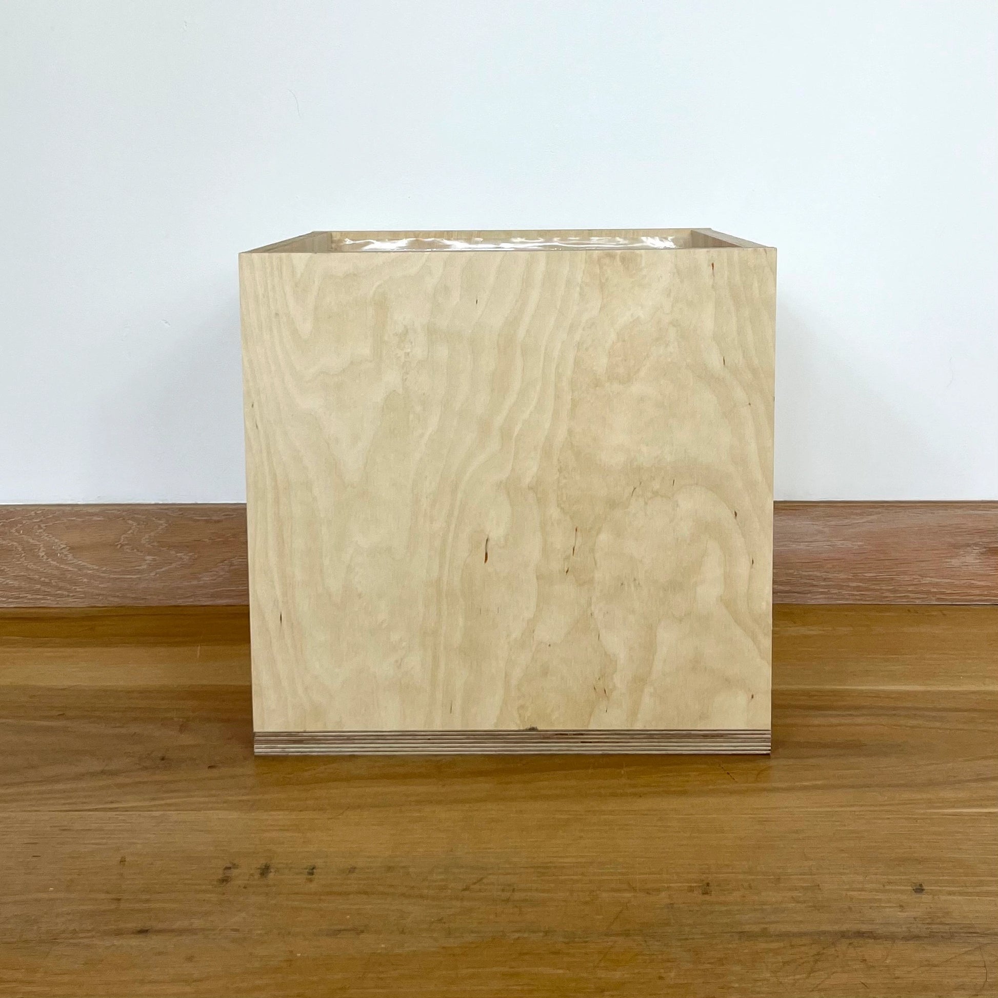 Simple pale wood storage box sits facing front on wooden floor.