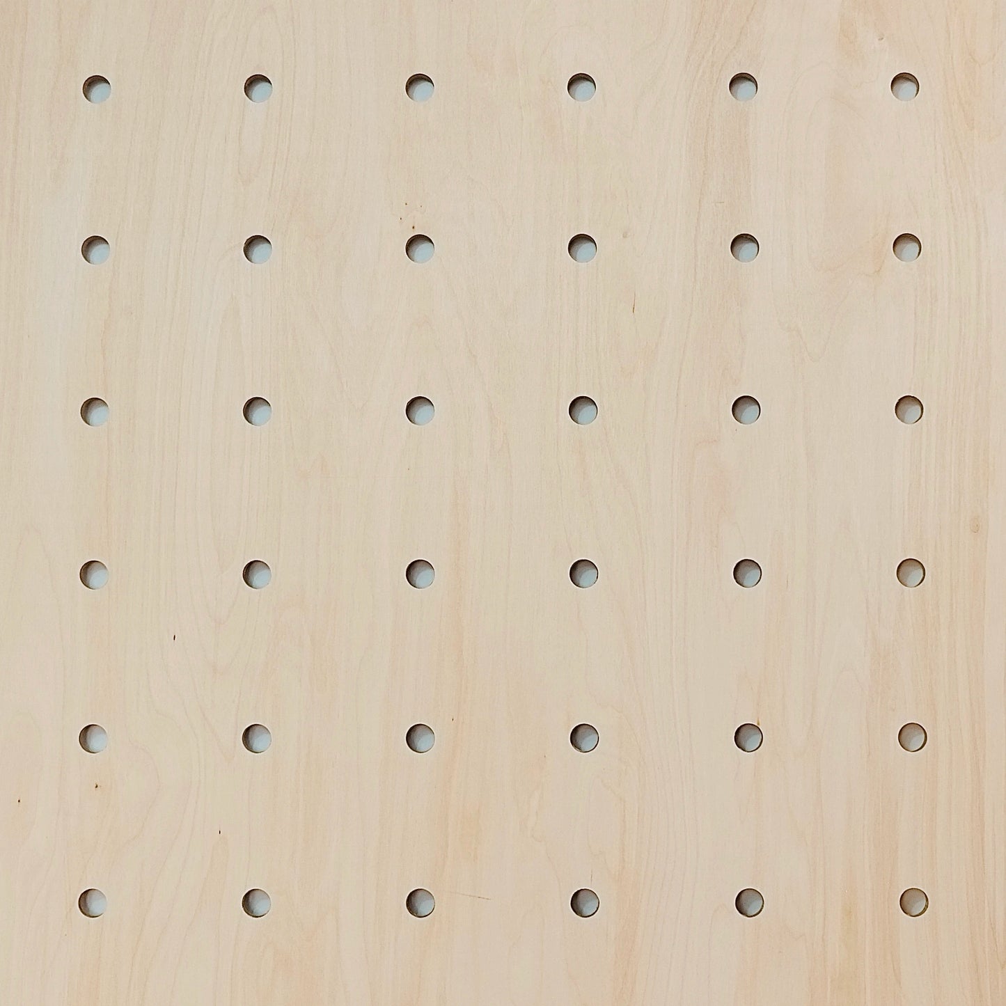 A close up of a pale wooden pegboard showing the round peg holes and the wood grain.