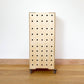 Birch plywood set of 3 stacking crates faces forward with 5 rows of vertical drill holes, 4 castors on base & wooden lid standing on a wood floor against a white wall.