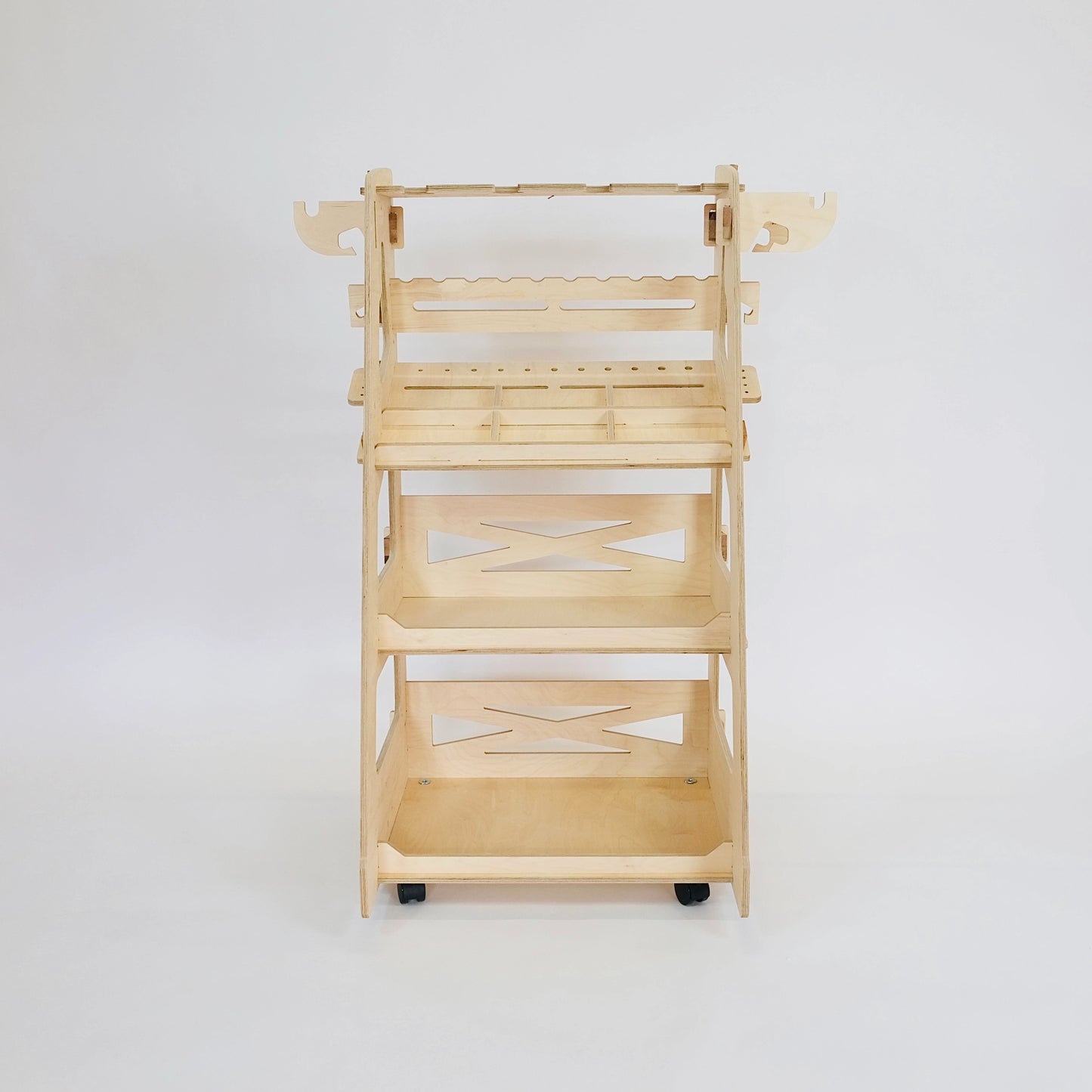 Front facing birch plywood tall tool trolley with 3 shelving trays, tool holding slots, 4 castors against a white background.