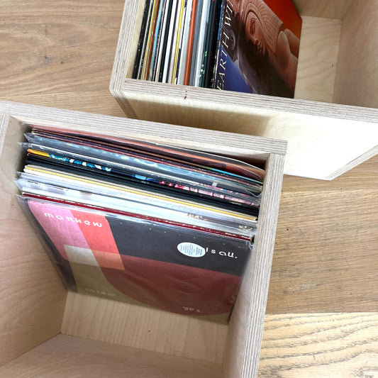 Birds eye view of two simple wooden storage boxes sitting on wooden floor, both display records.