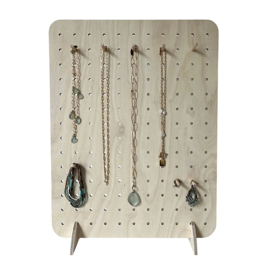 Pale wooden pegboard faces to front displaying various pieces of jewellery.