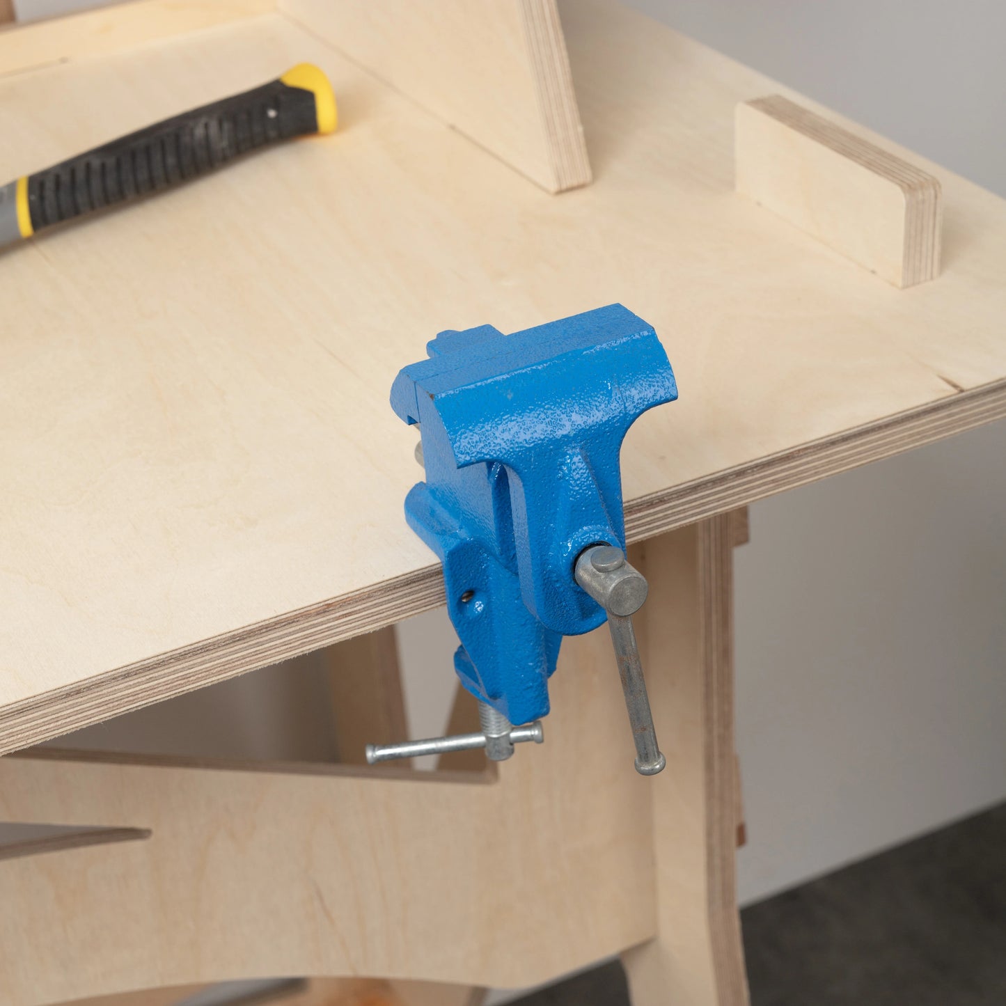 A close up of a pale wooden work bench showing detail and layers of the plywood, and  a blue vice.