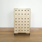 A front facing stack of two birch plywood stacking square crates with castors, 5 rows of vertical drilled holes on front & wooden lid, standing on a wooden floor infront of a white wall.