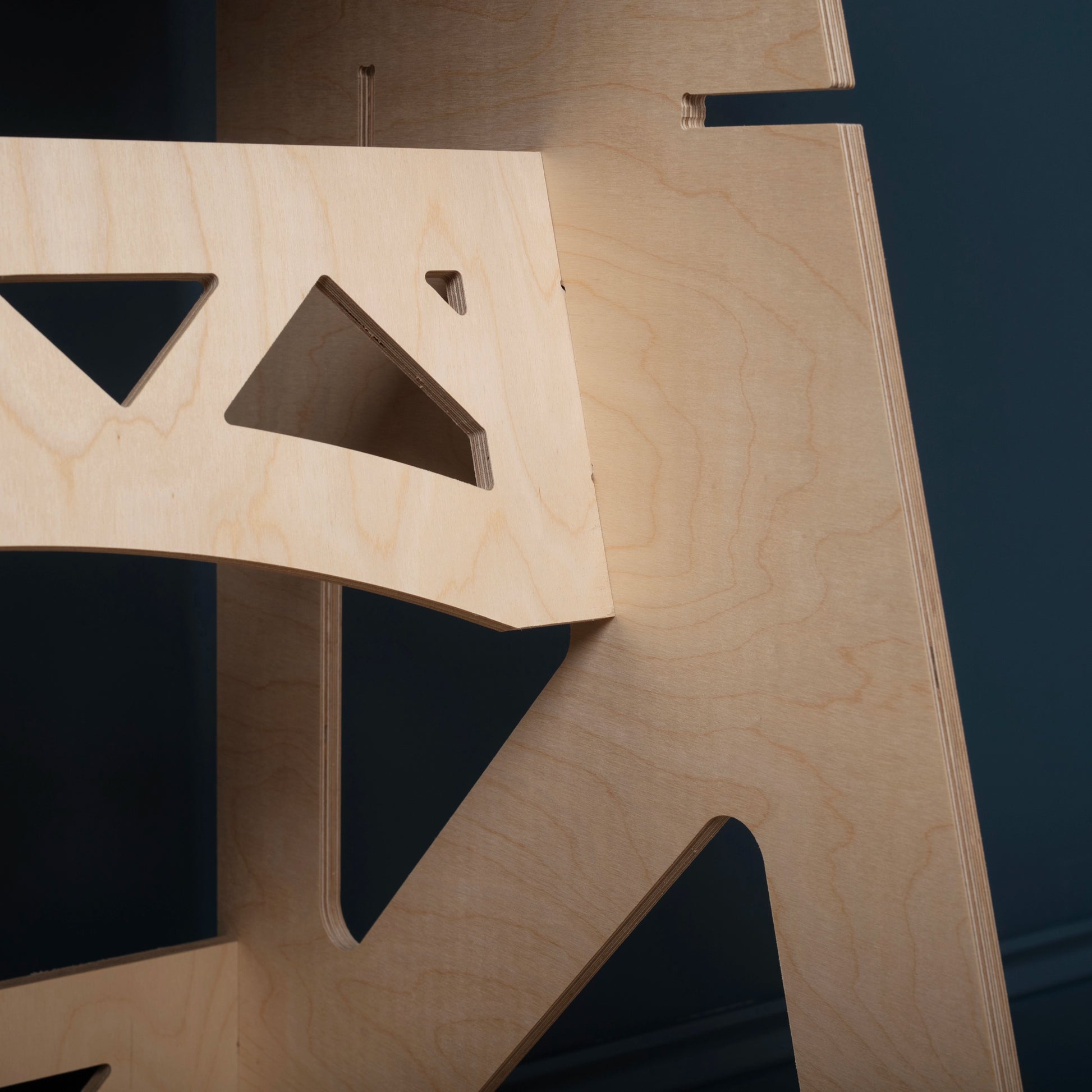 close up of triangle cut outs on birch plywood stand up/sit down desk against a dark blue wall