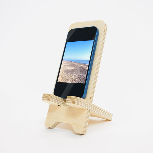 wooden pale birch plywood phone stand with phone sitting angled to the left on a white background. 